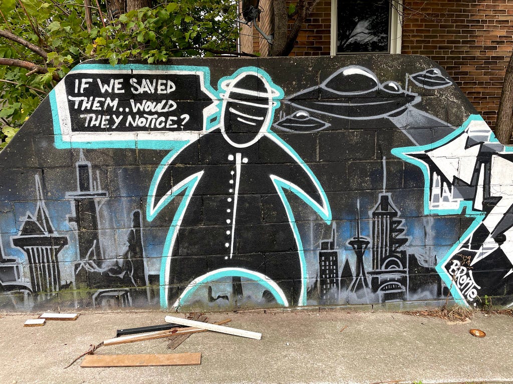 Mural artwork featuring a black blob person with the thought bubble, “If we saved them…would they notice?” while UFOs attack a city.