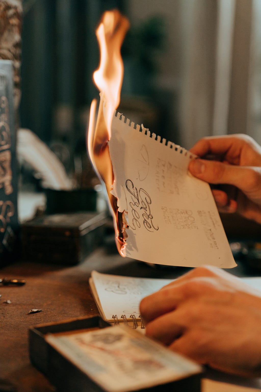 A person’s hand holding a diary page with some text on it, the paper is burning at one end