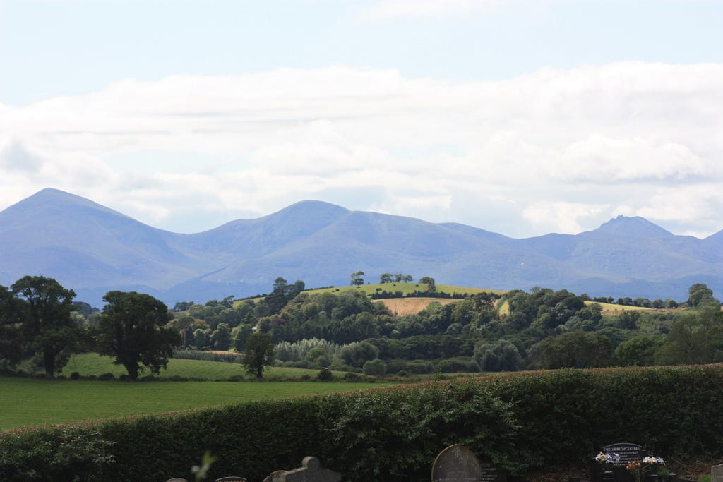 Mourne Mountains. Countryside with shadowy mountains looming over in the far distance with bright white and airy clouds.
