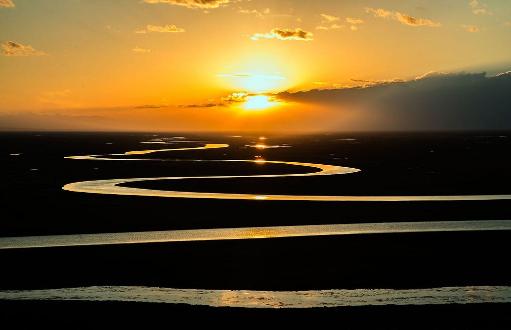 A winding river, with the sun going down behind the plains.