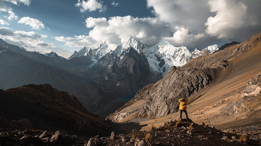 A Man Stands on a mountain staring at a much larger mountain.