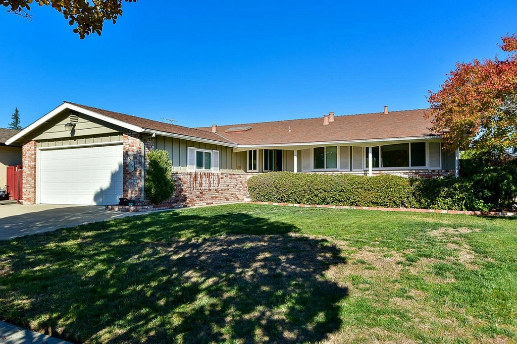 A ranch-style, part-brick home with a front yard on a sunny day.