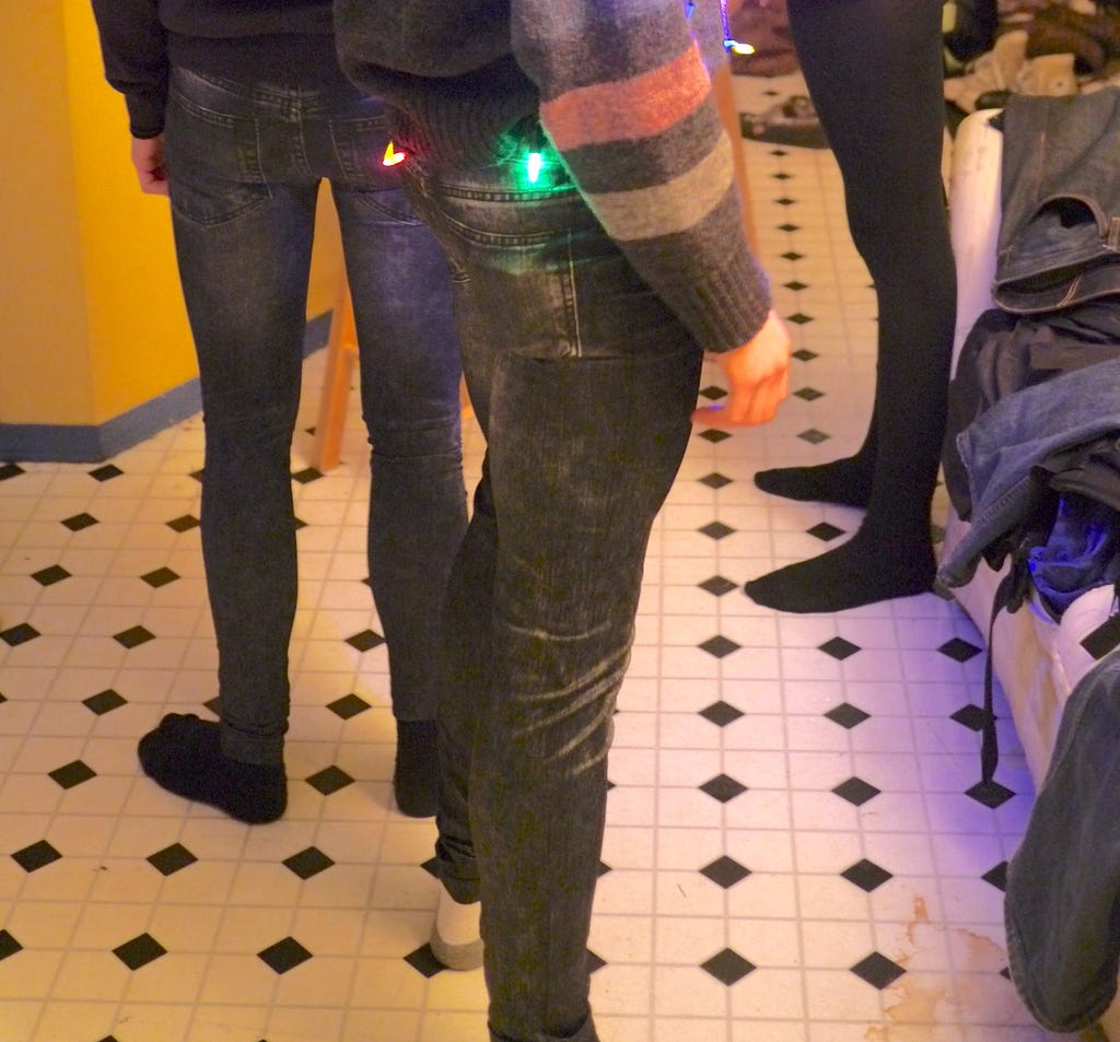 A picture from a holiday party of me in jeggings, and a sweater with LED lights on top. More jeggings in the backgrouns, and a pile of jeans on a couch.