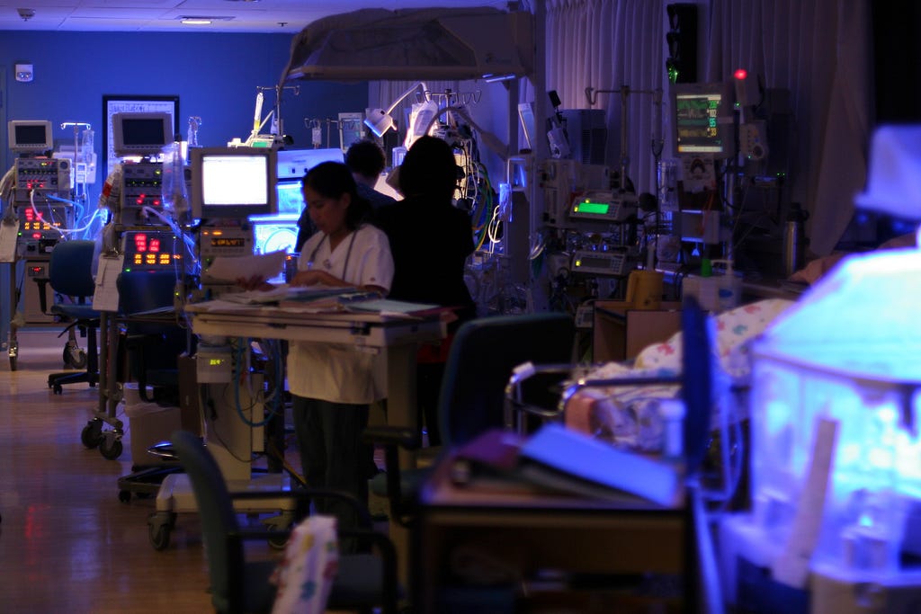 A large, darkly lit room with many glowing machines. Several doctors and nurses are visible.