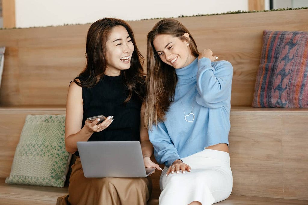 two women sit together smiling as they discuss sex happily and freely.