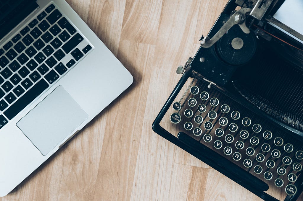 A new laptop on the left and an antique typewriter on the right