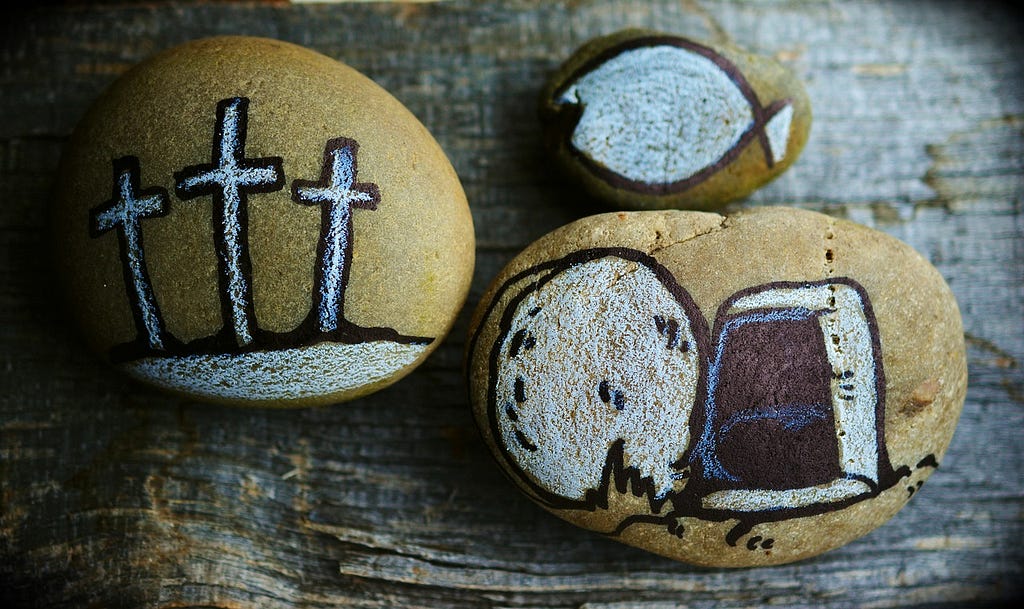Three rocks painted. One with three crosses. One with a fish symbol. and the last one with the empty tomb of Jesus, a sign of the resurrection. By Pixabay