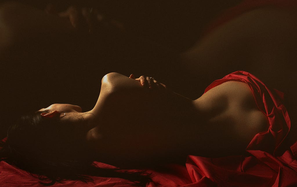 A woman half-naked in red laying in bed with her arms wrapped around her body.