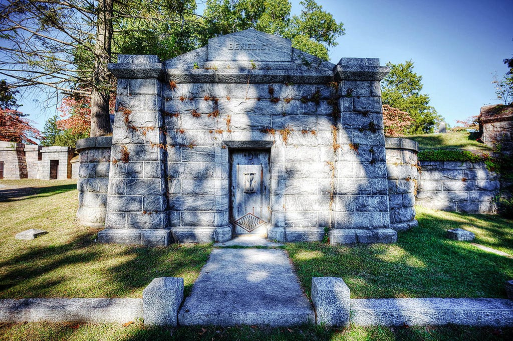 Close-up view of a stone mausoleum with a wooden door, located in Sleepy Hollow Cemetery. The inscription “Benedict” is etched above the door.