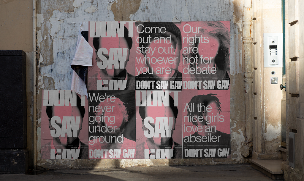 A series of distressed posters on a wall with pink blank faces. The posters says Don’t Say Gay in big white text
