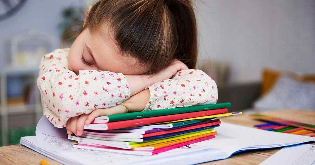 Little girl falling asleep at her desk on top of her school workbooks.