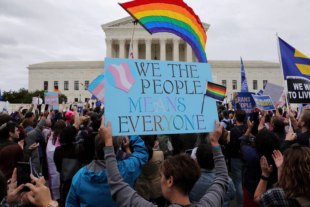 LGBT activists at the U.S. Supreme Court in Washington, D.C. The sign being held in the forefront reads “we the people means everyone” on a sky blue background.