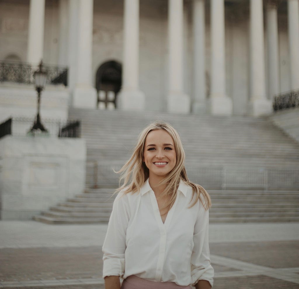 A young woman smiling and standing in front of the United States Capitol