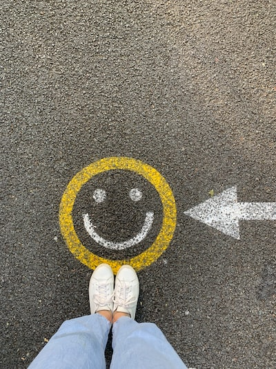 person standing beside a chalk smiley drawn on the asphalt with an arrow pointing to it