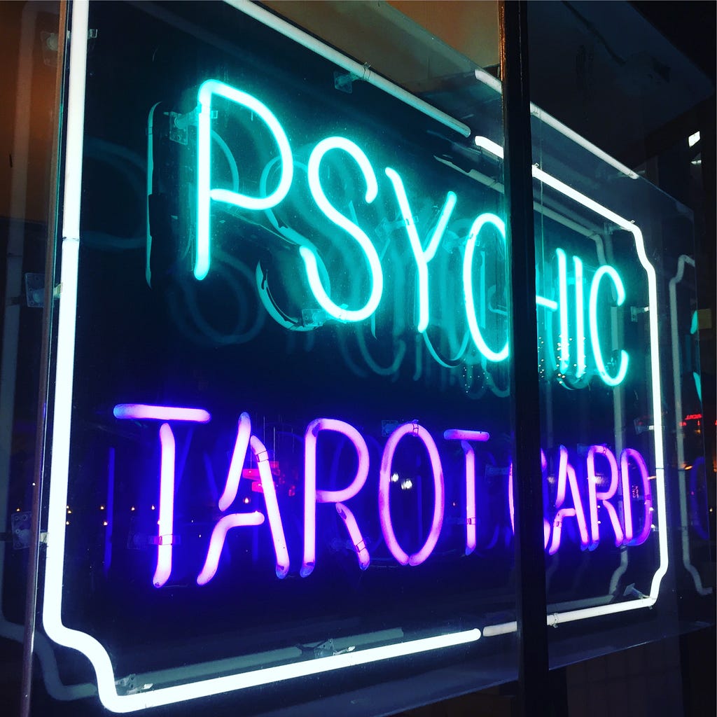 A neon sign in a shop window blares the words “PSYCHIC TAROT CARDS”