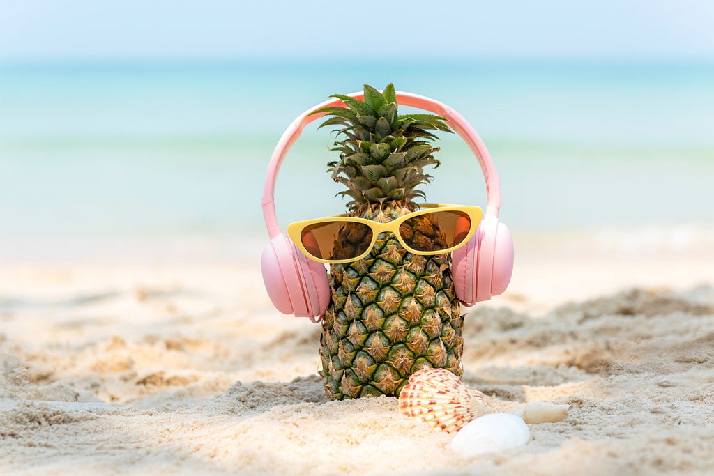A pineapple on a beach with yellow sunglasses and pink headphones.