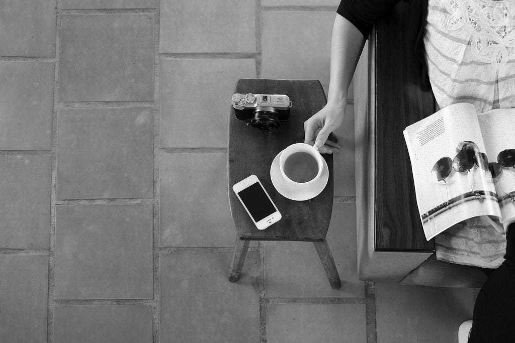 Woman seated on sofa perusing a catalog while drinking tea.