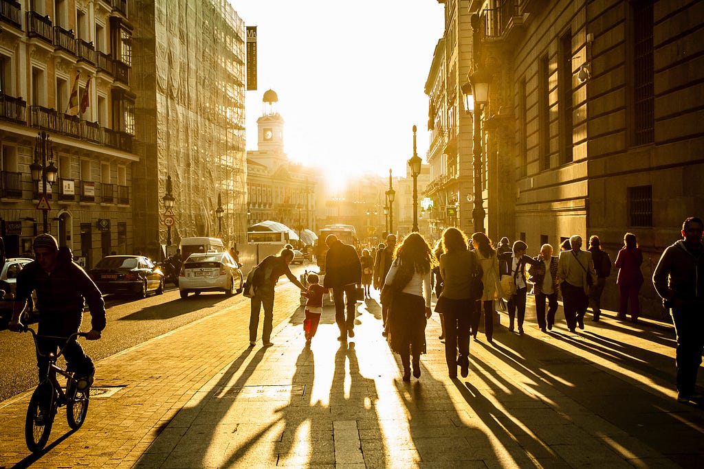 Backside of people of all ages walking and riding bikes on street in Madrid, Spain, with the glow of the sun