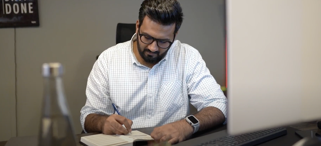 A man writing in his notebook at a desk.