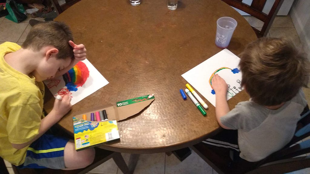 Two kids drawing rainbows at the kitchen table.