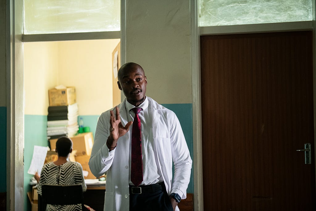 A doctor in a white coat stands inside a healthcare facility.