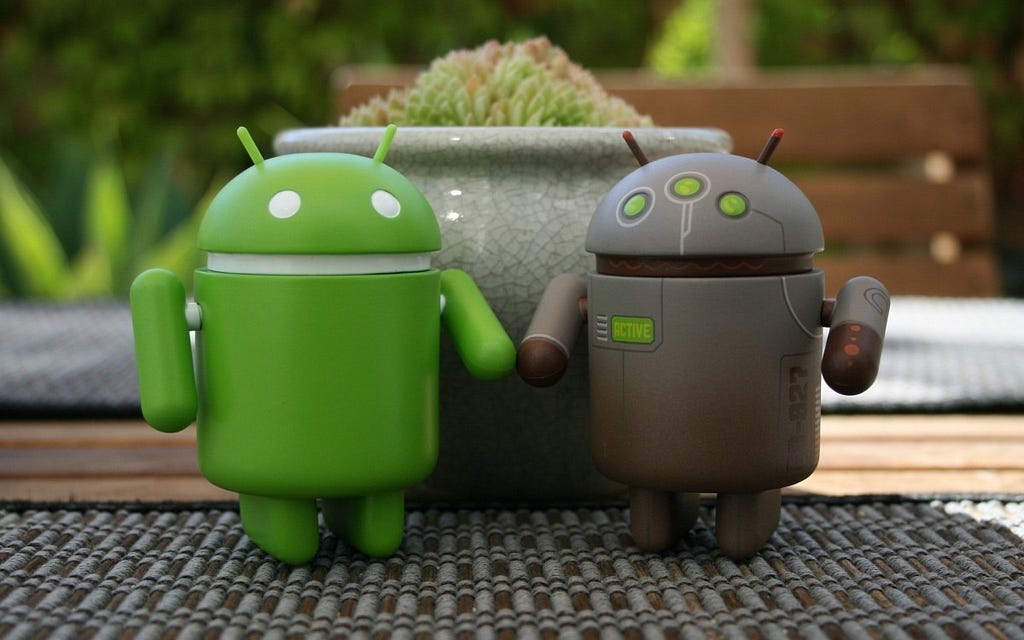 a green clay model of android bot and a earthen colored clay model of another android bot are standing next to each other on a table.