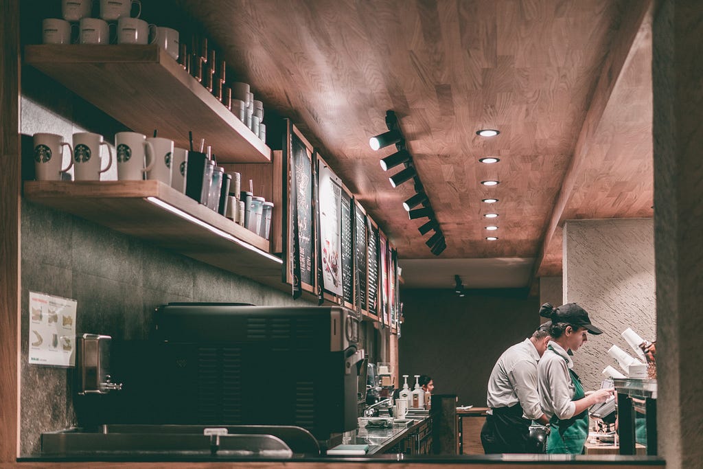 A look behind a Starbucks counter where two StarBucks employees can be seen working on an order.