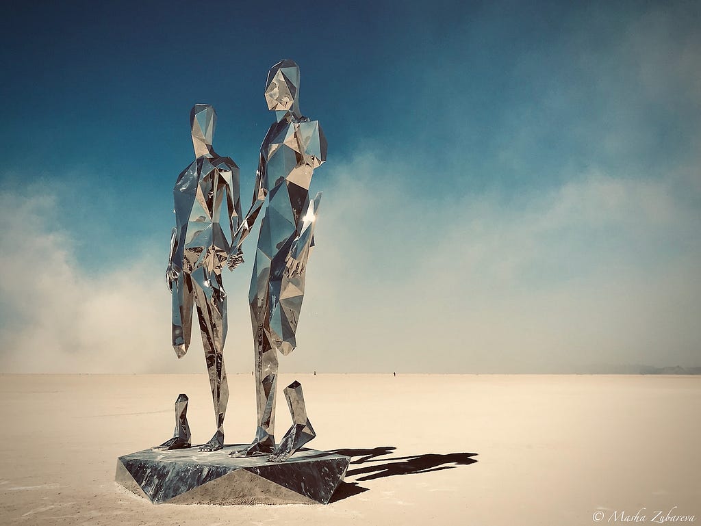 An art installation representing two human figures holding hands, made of mirrors, in the middle of Nevada Desert.
