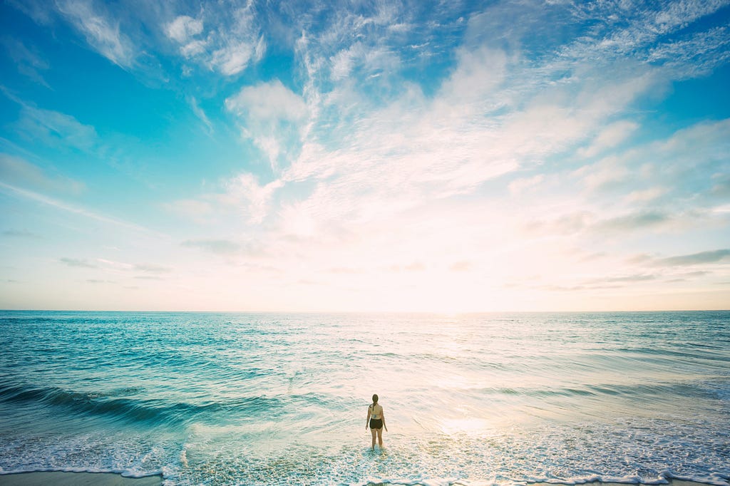 pessoa no meio do mar olhando para o infinito e o sol está nascendo