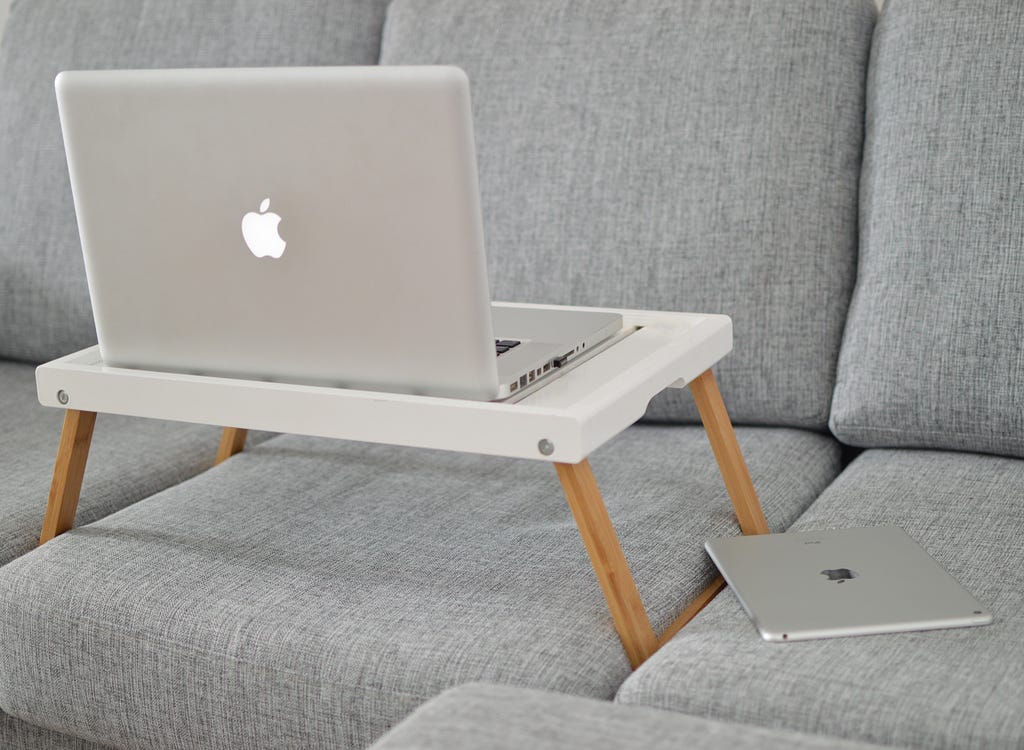 A laptop and iPad sitting on a couch. The laptop is on a portable desk.