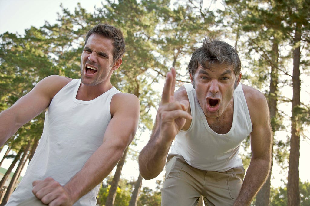 Two men in shirts, one of them is pointing his finger at the camera and screaming