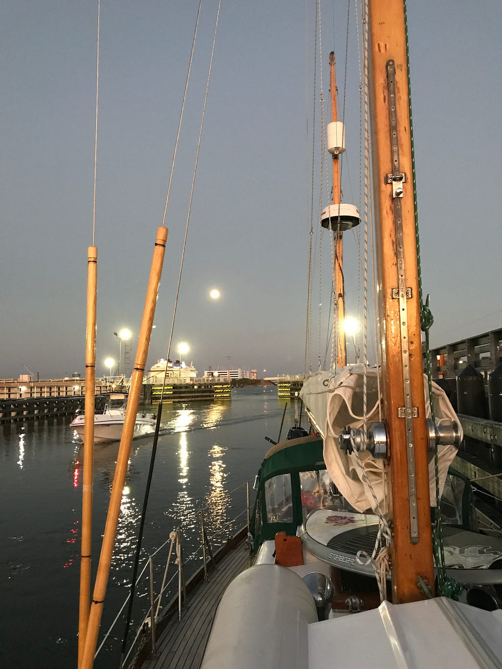 The sails of a boat and lights on the water inside a lock.