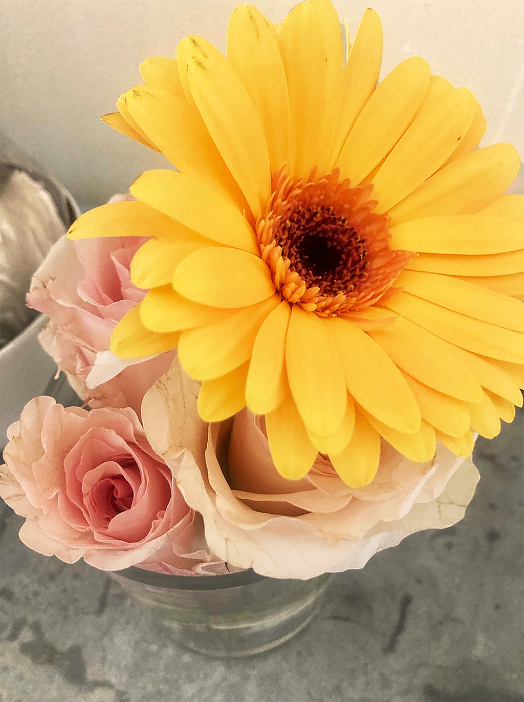 An arrangement of yellow Gerbera daisy and pale pink roses in a vase.