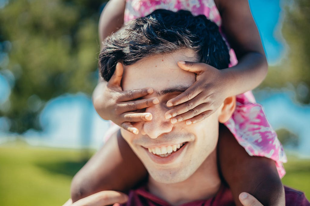 Close-up Photo of a Kid covering man’s eyes, he is smiling.