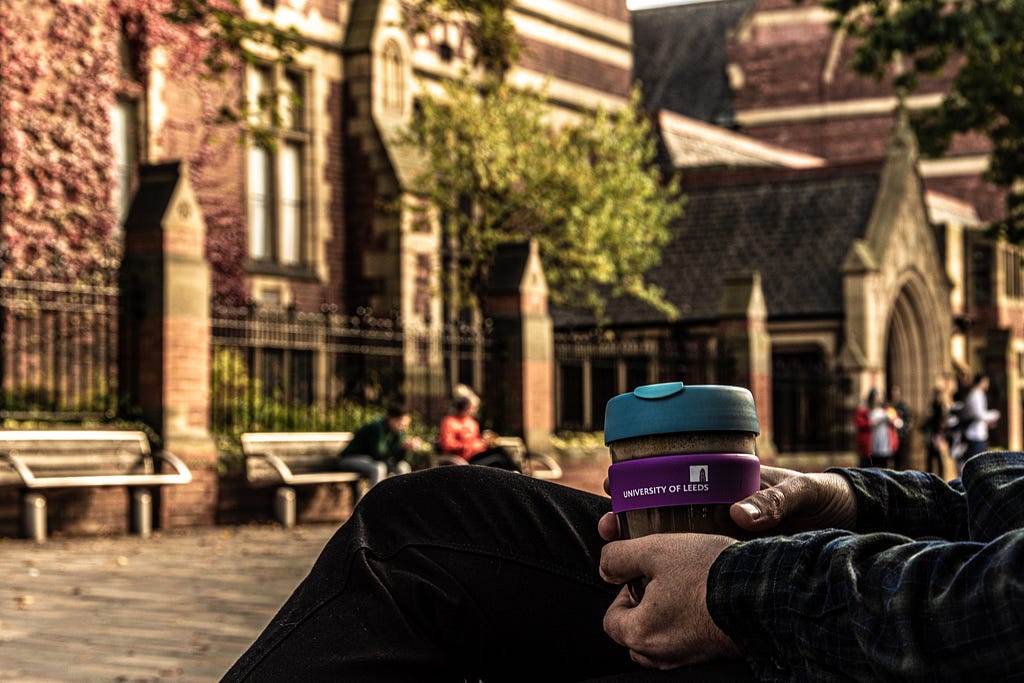 someone holding a coffee mug sitting outside the Great Hall on a sunny day
