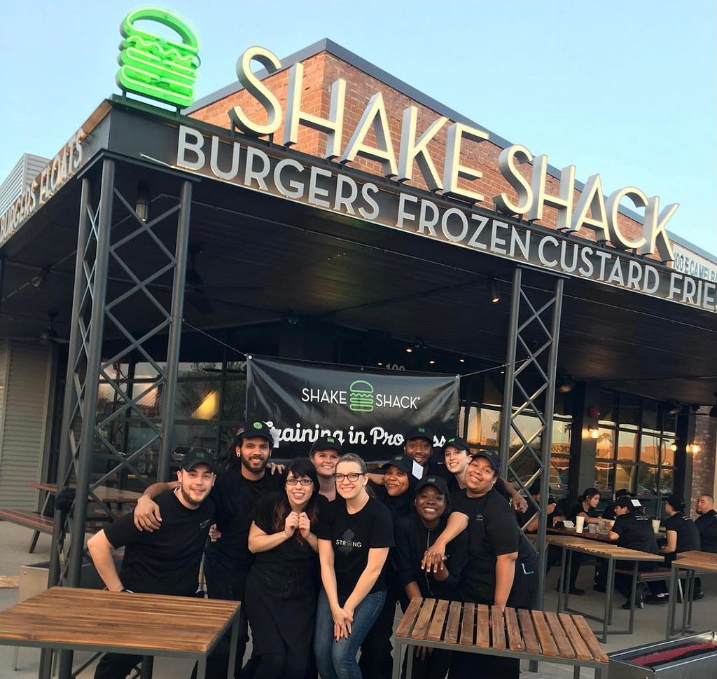 A group of people standing under a “Shake Shack” banner in front of a store.