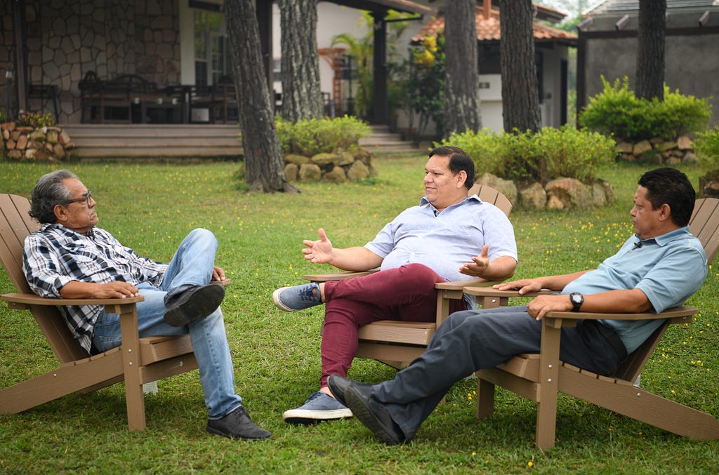 Tres hombres hondureños adultos discuten formas de apoyar a la comunidad LGBTQI+ mientras un camarógrafo filma la conversación.
