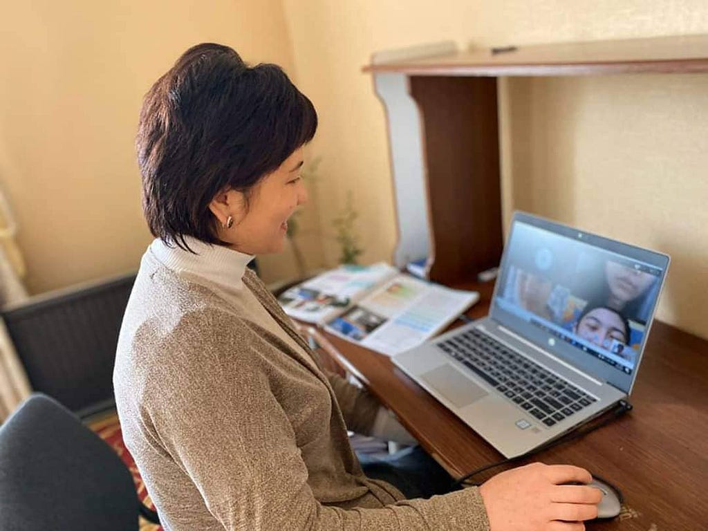 A woman sits in front of a laptop showing a virtual meeting.