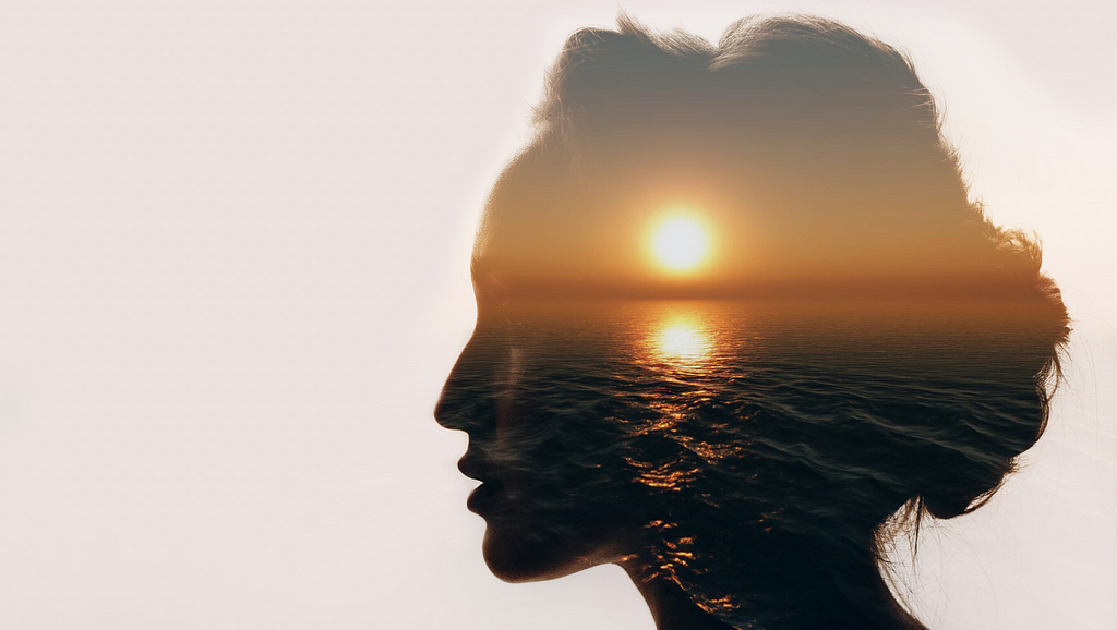 silhouette of woman’s head with a sunset over the water projected on it