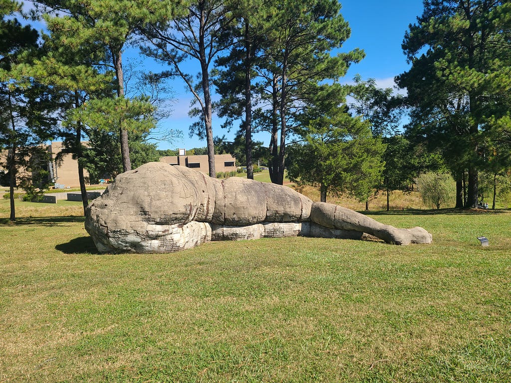 Concrete and steel sculpture depcits human form laying on its side