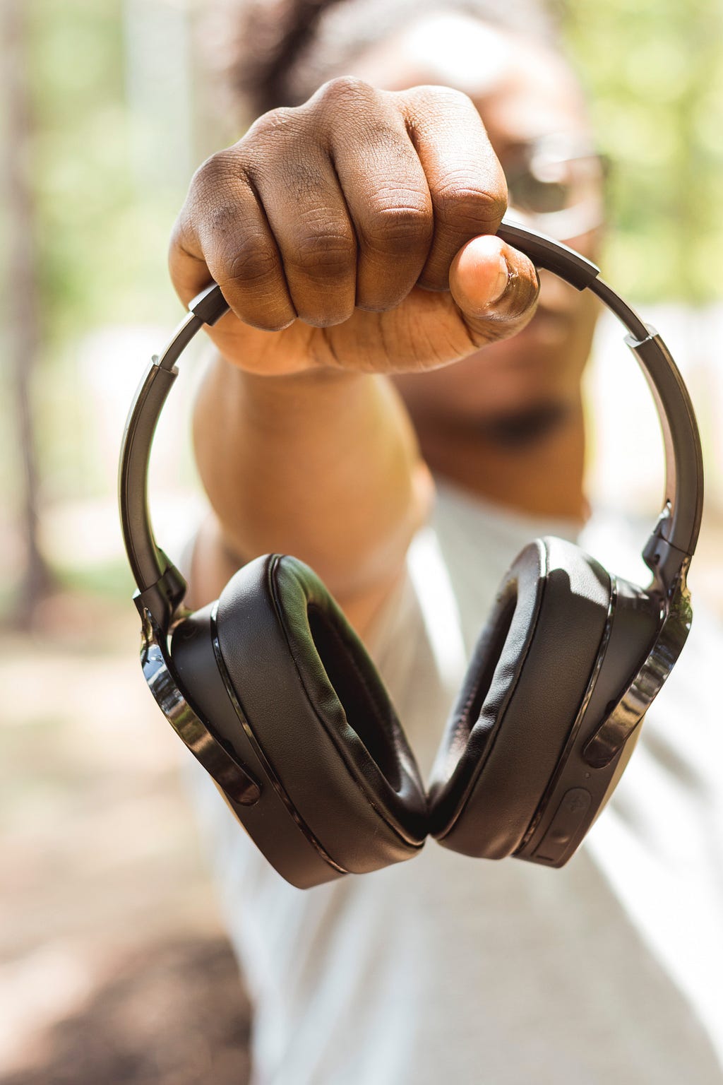 Homem negro desfocado com o braço esticado oferecendo um fone de ouvidos