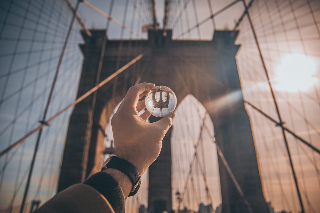 Picture of a bridge with a hand holding a glass sphere, inside the sphere the bridge shows upside down