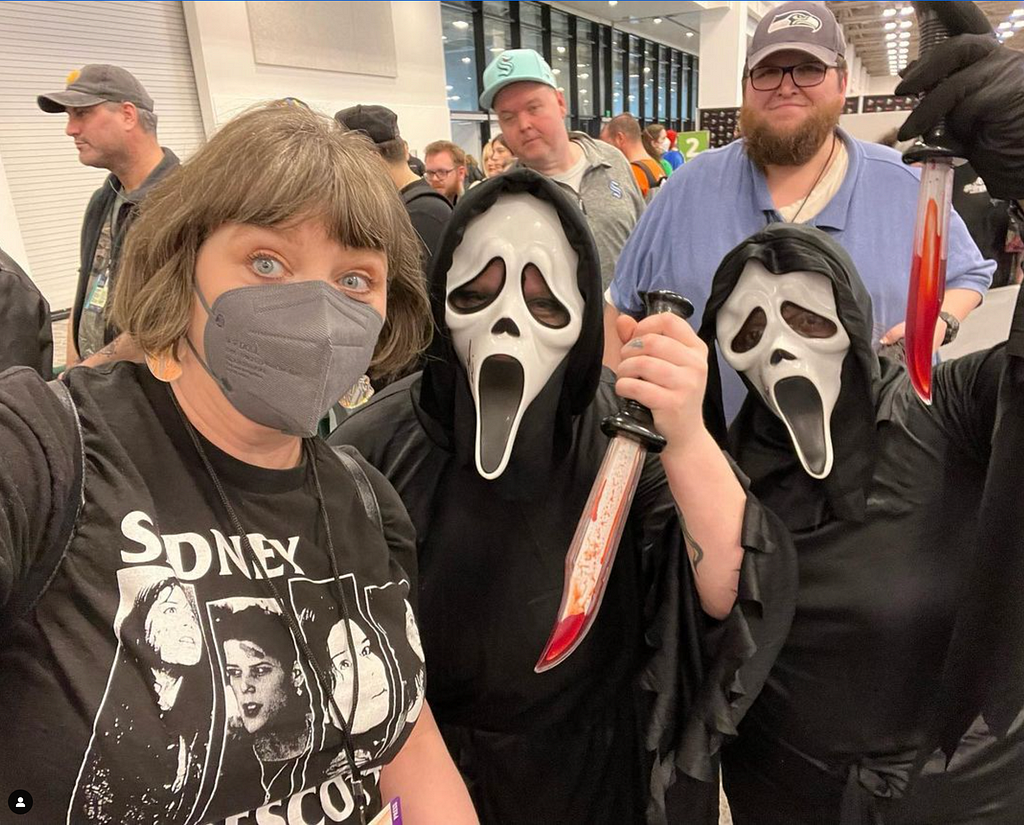 A woman poses with two people in Scream costumes at ECCC