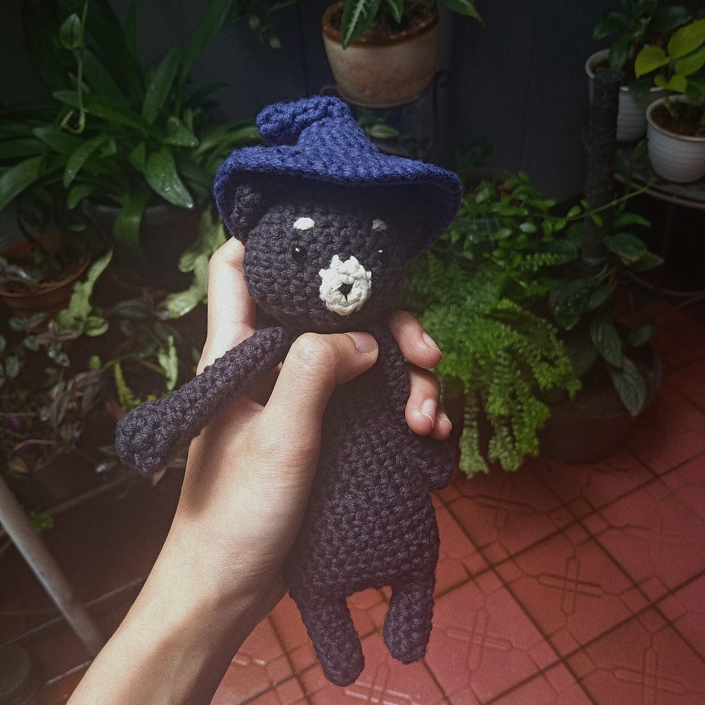 A crocheted bear wearing a purple witch hat.