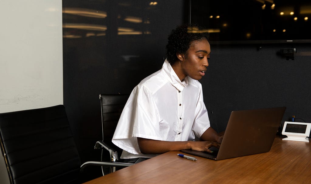 A black, non-binary person using a laptop at work