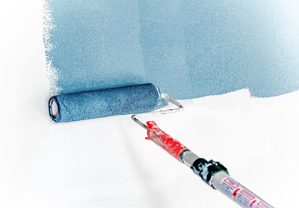 A paint roller applying blue paint to a white wall.