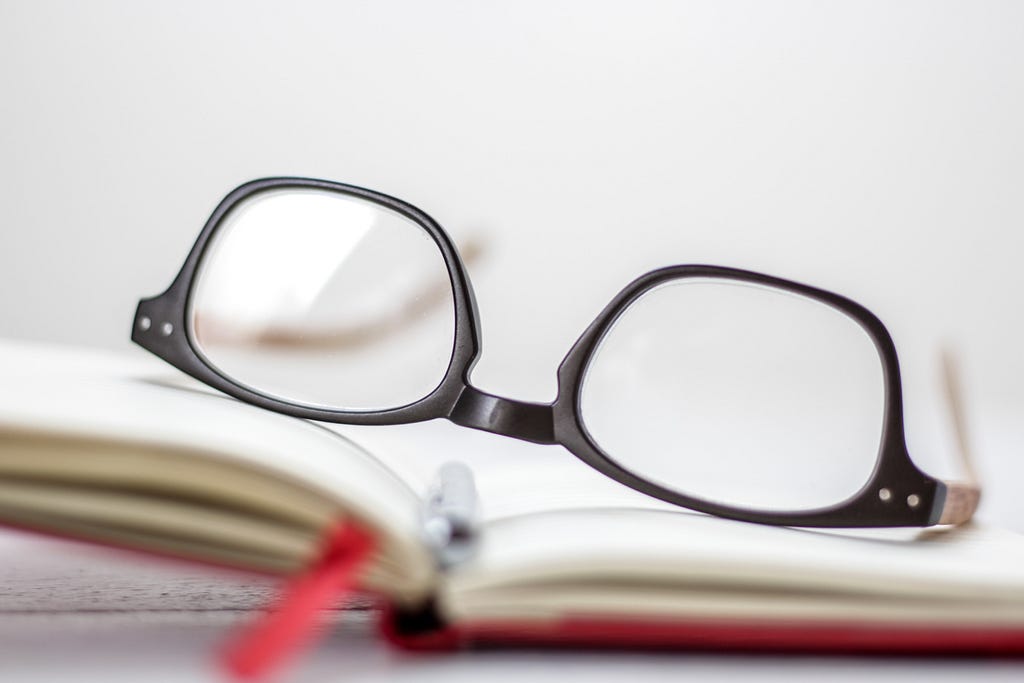 Photo of glasses laid on an open notebook with a red ribbon bookmark