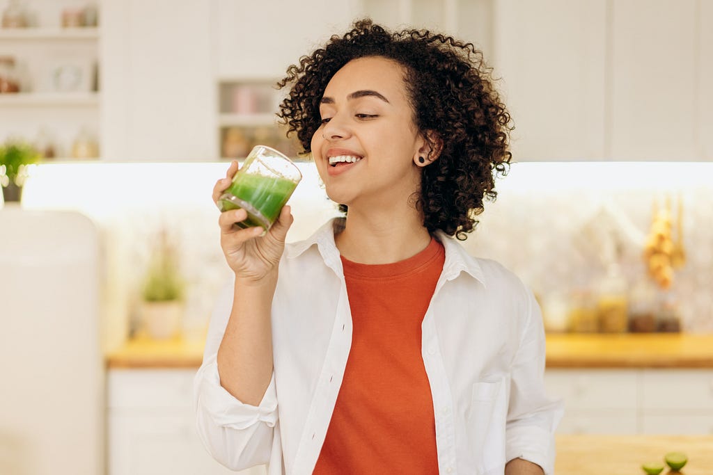 A woman who is making detox with a green juice while smiling