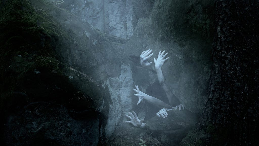 A picture of pale arms and hands reaching out of a dark cave.