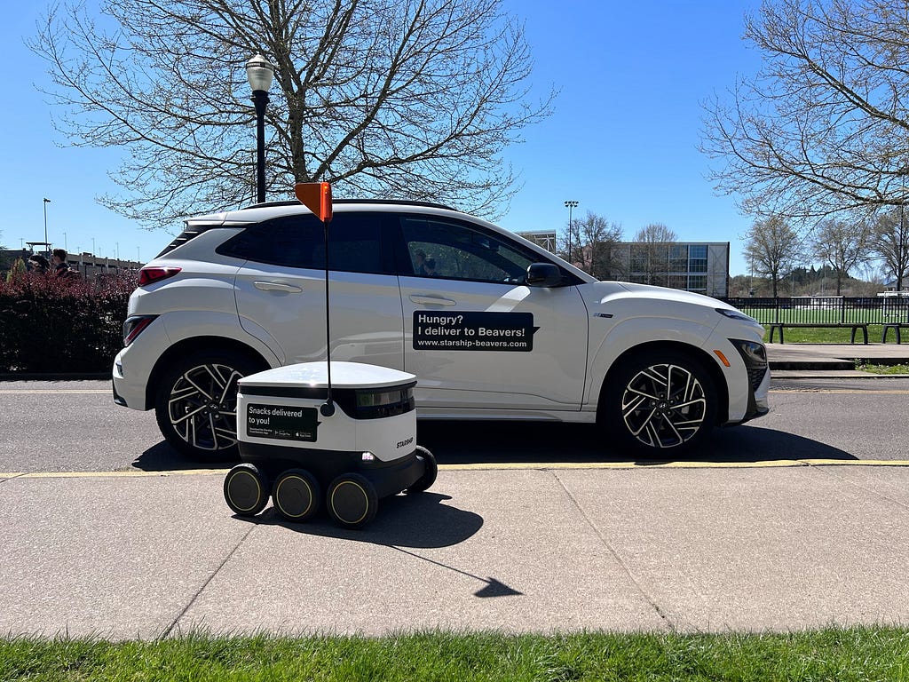 A Starship Delivery Robot next to Henry’s vehicle dressed up like a larger version of the delivery robot